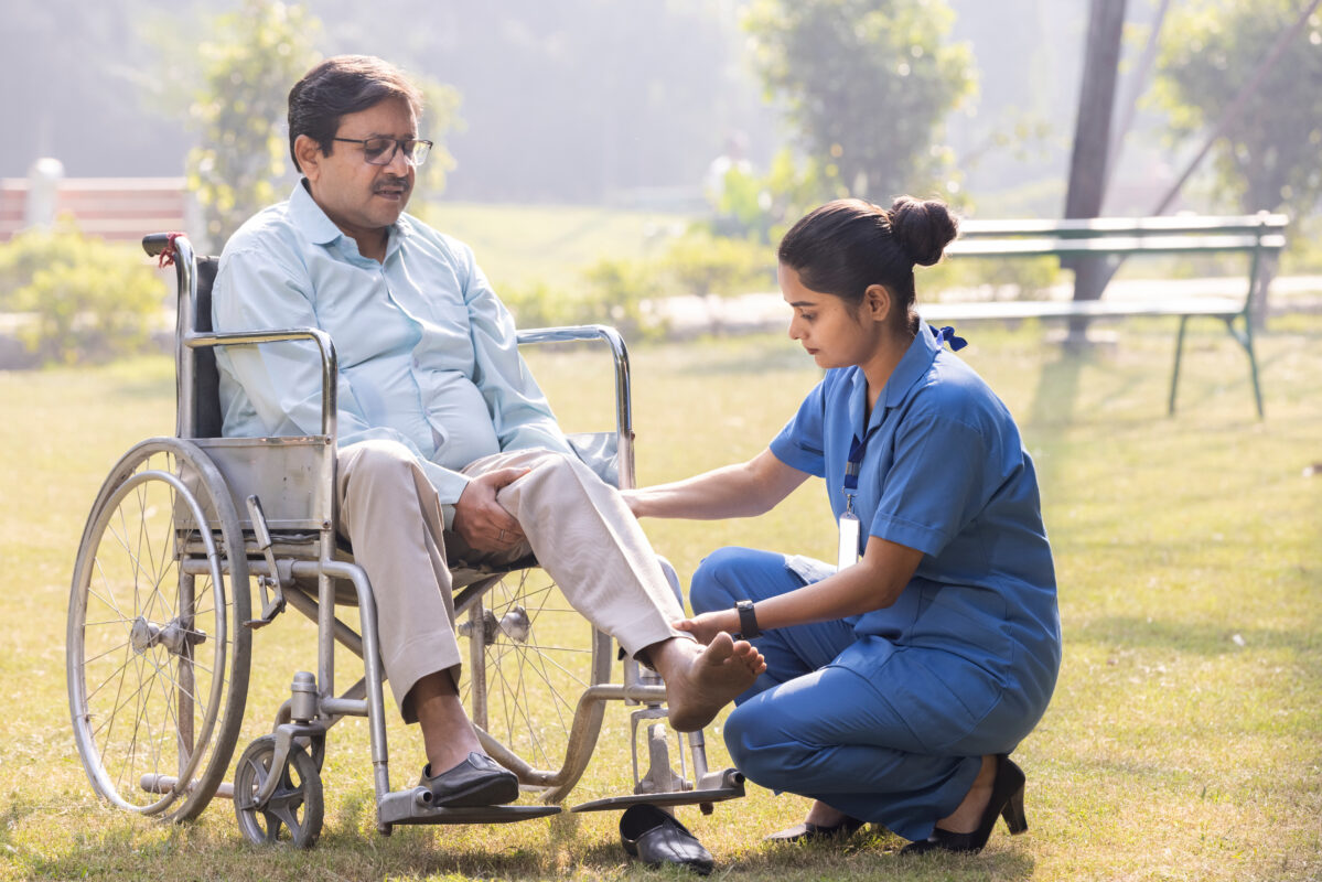 Female nursing worker helping senior man doing exercise at park.